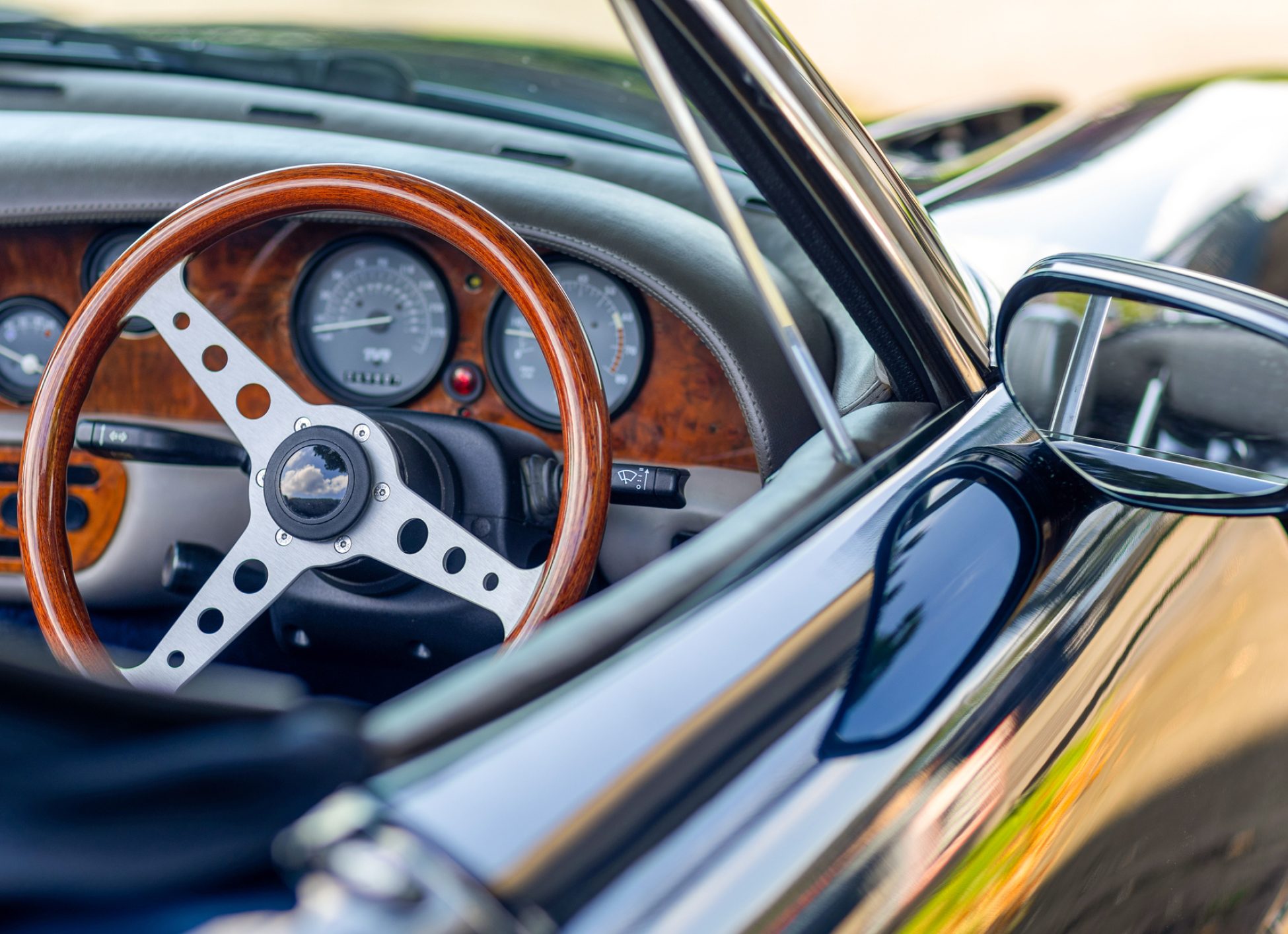 Beautiful wooden steering wheel and and old-fashioned small gauges and large beautiful exterior mirror of a historic cabriolet - right-hand drive
