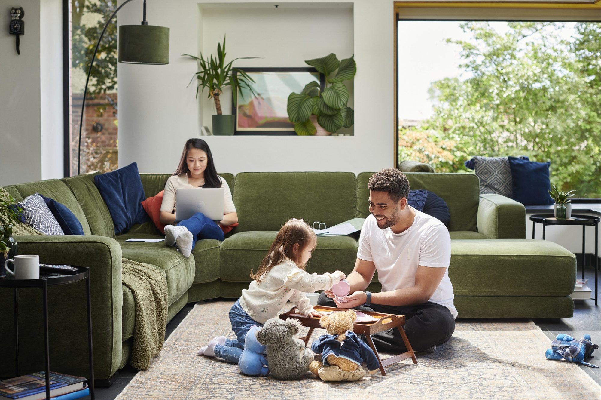 little girl has a teddy bear tea party with dad in the living room whilst mum catches up on some work