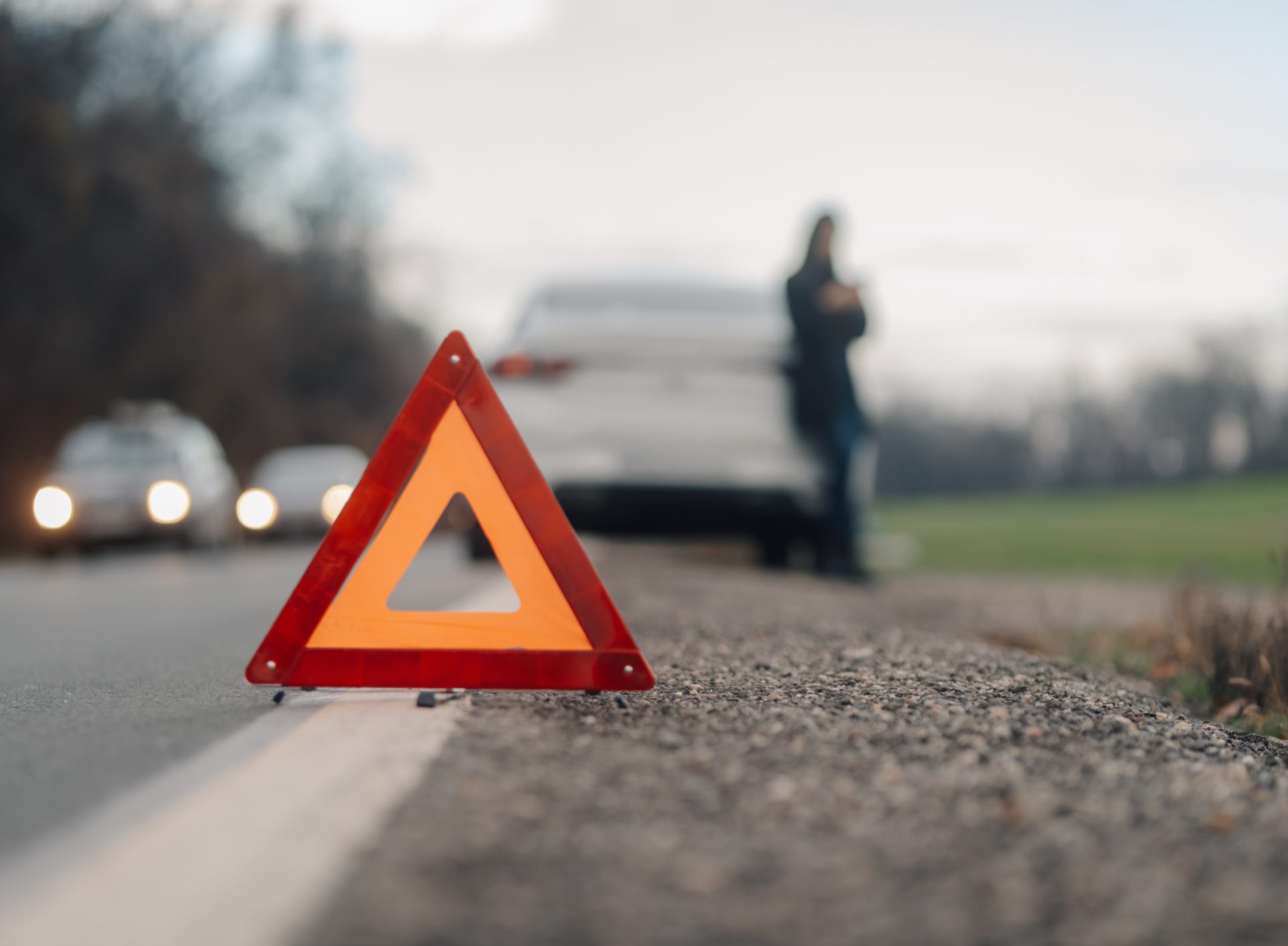 Driver waiting for assistance after placing warning triangle on a country road next to broken down car