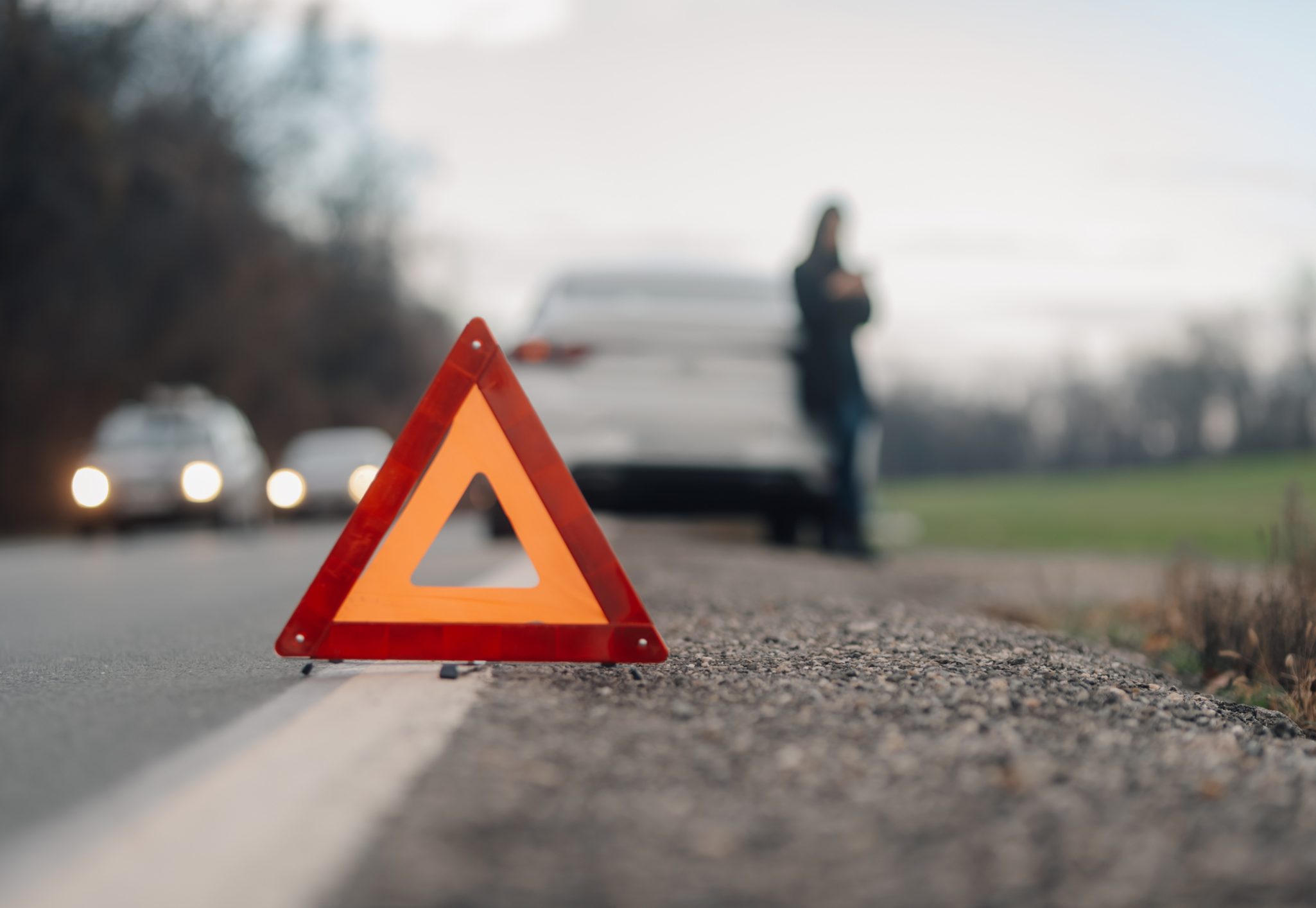 Driver waiting for assistance after placing warning triangle on a country road next to broken down car
