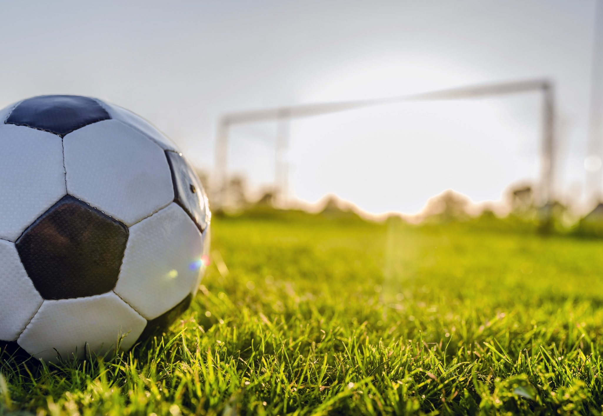 Photo of Traditional Leather, black and white soccer ball on soccer field or stadium in the sunset day before the match, with Soccer goalpost as background