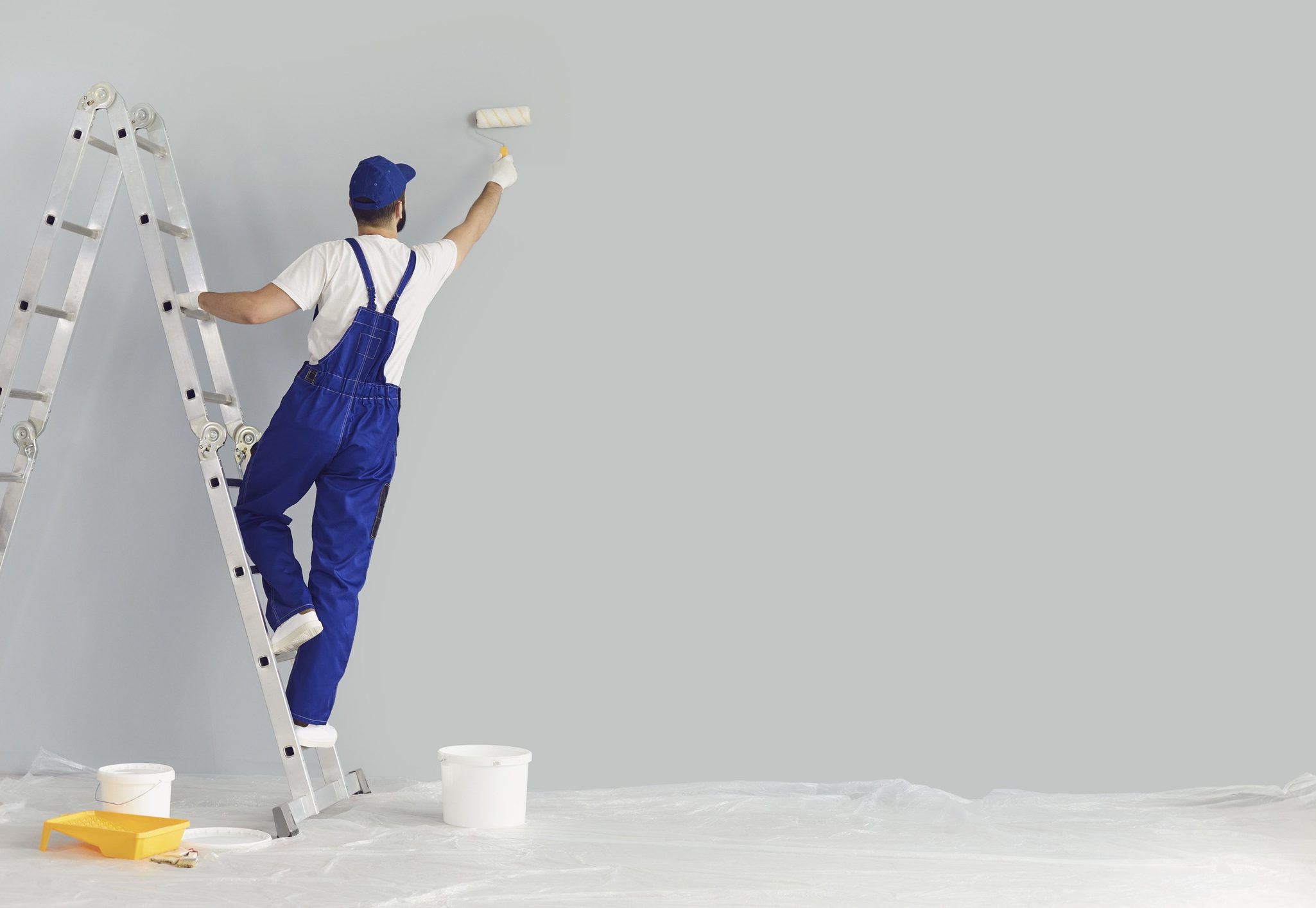 Building contractor painting grey wall with roller brush, copy space text. Back view of young construction worker renovating house